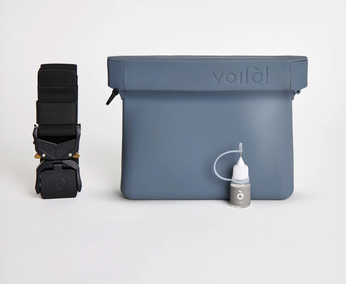 Gray pouch with black strap and bottle of oil on a white background.
